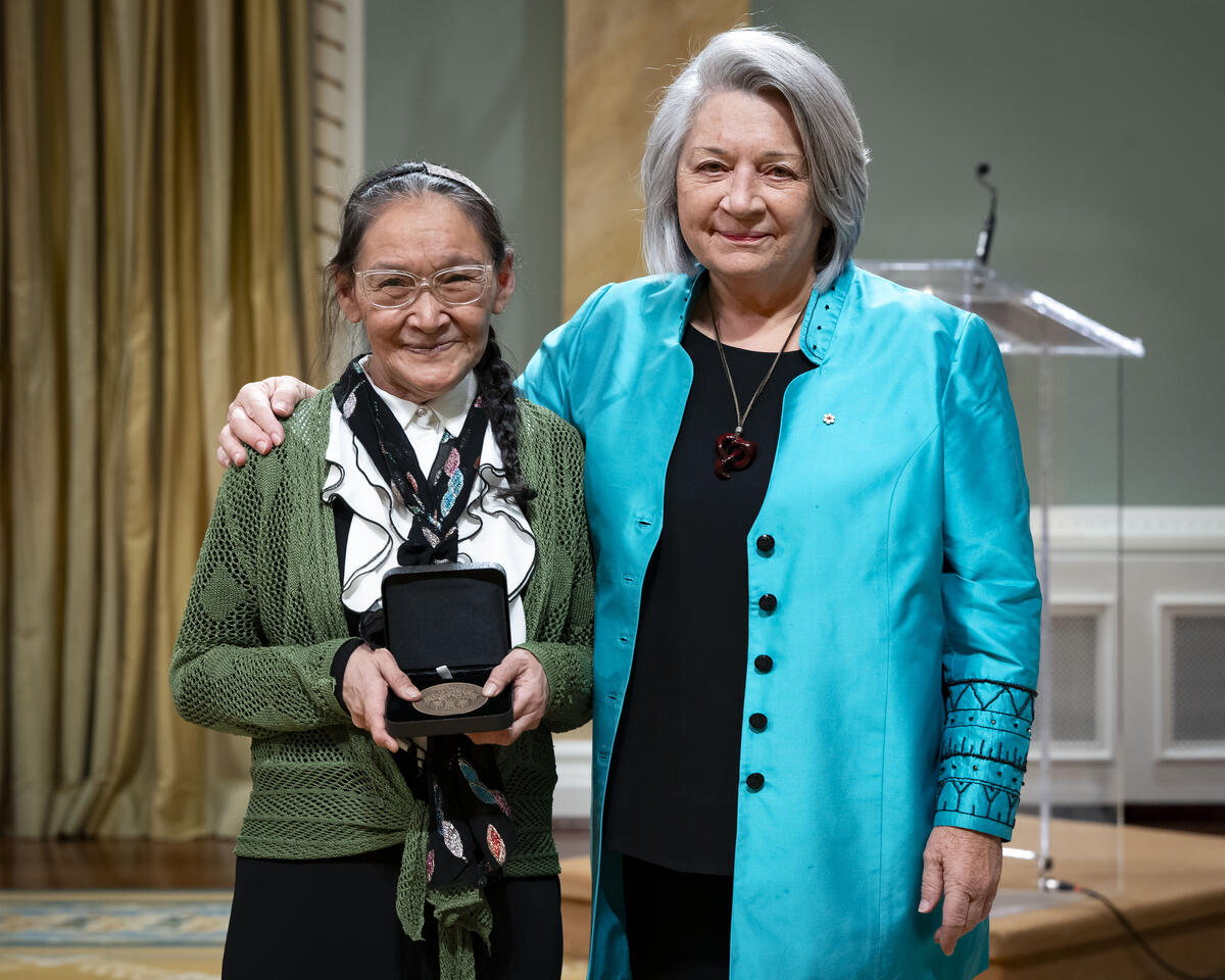 La gouverneure générale Mary Simons pose avec une dame qui tient un coffret de médailles ouvert.