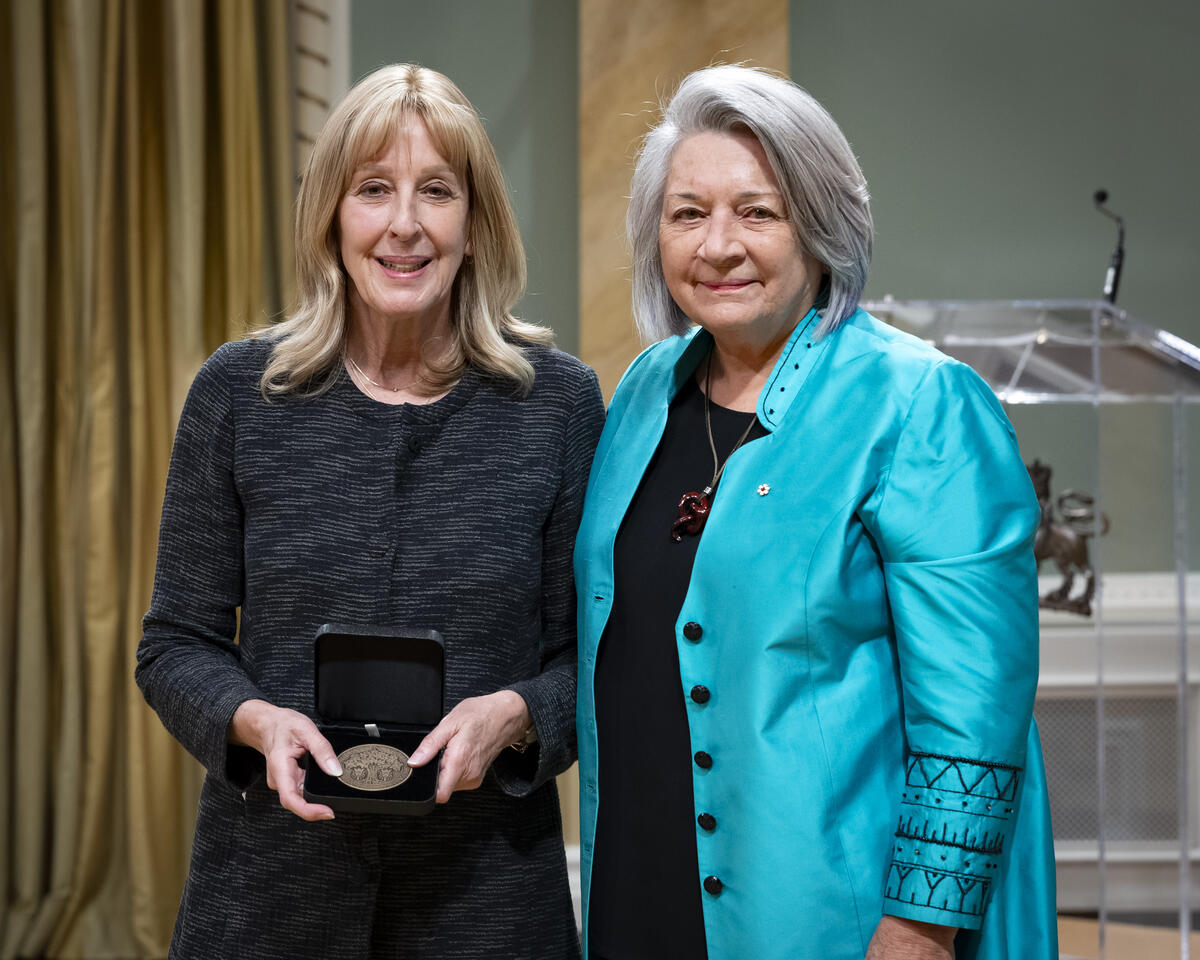 La gouverneure générale Mary Simons pose avec une dame qui tient un coffret de médailles ouvert.