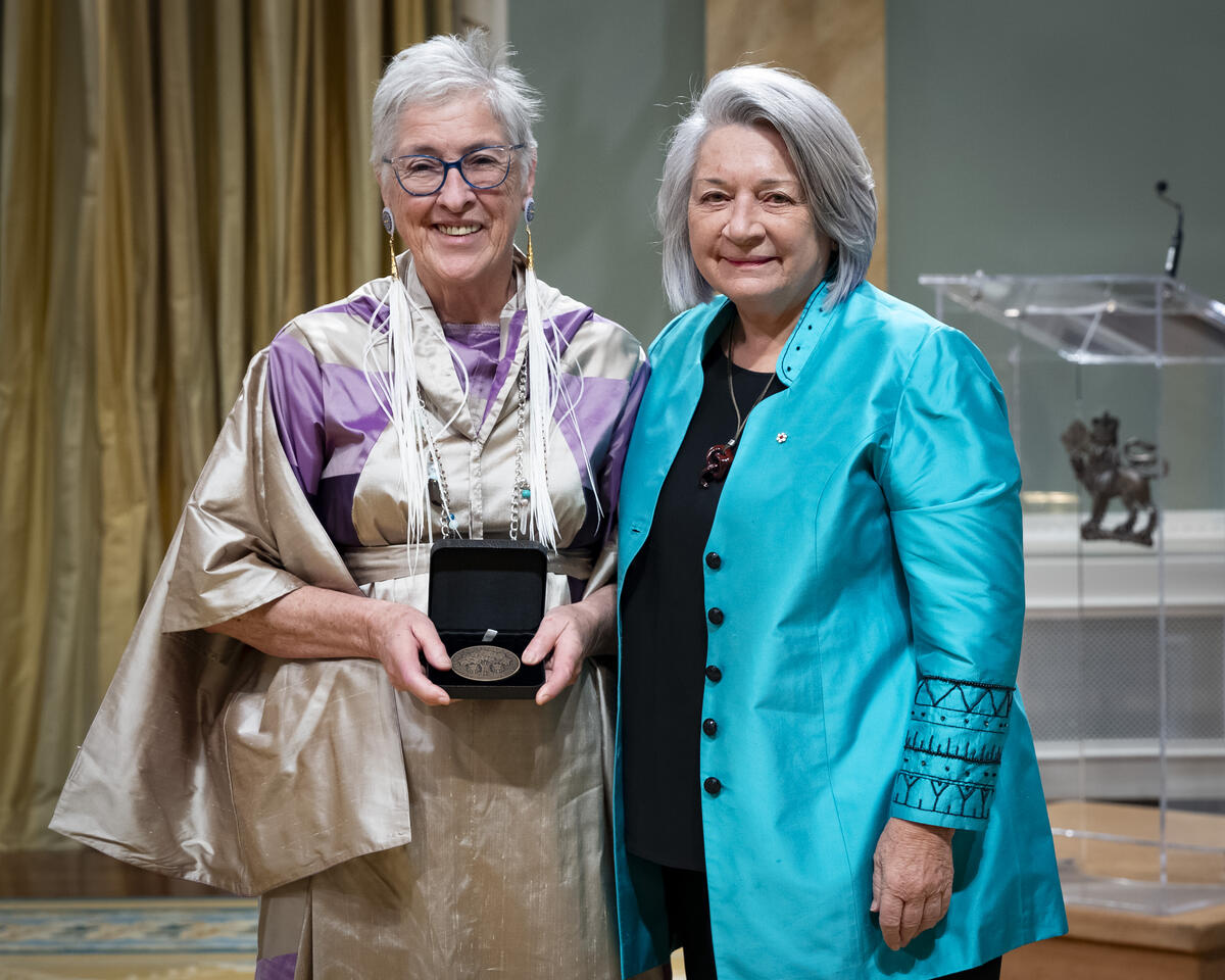 La gouverneure générale Mary Simons pose avec une dame qui tient un coffret de médailles ouvert.