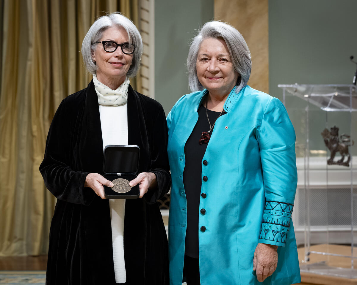 La gouverneure générale Mary Simons pose avec une dame qui tient un coffret de médailles ouvert.