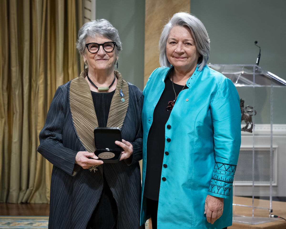 La gouverneure générale Mary Simons pose avec une dame qui tient un coffret de médailles ouvert.