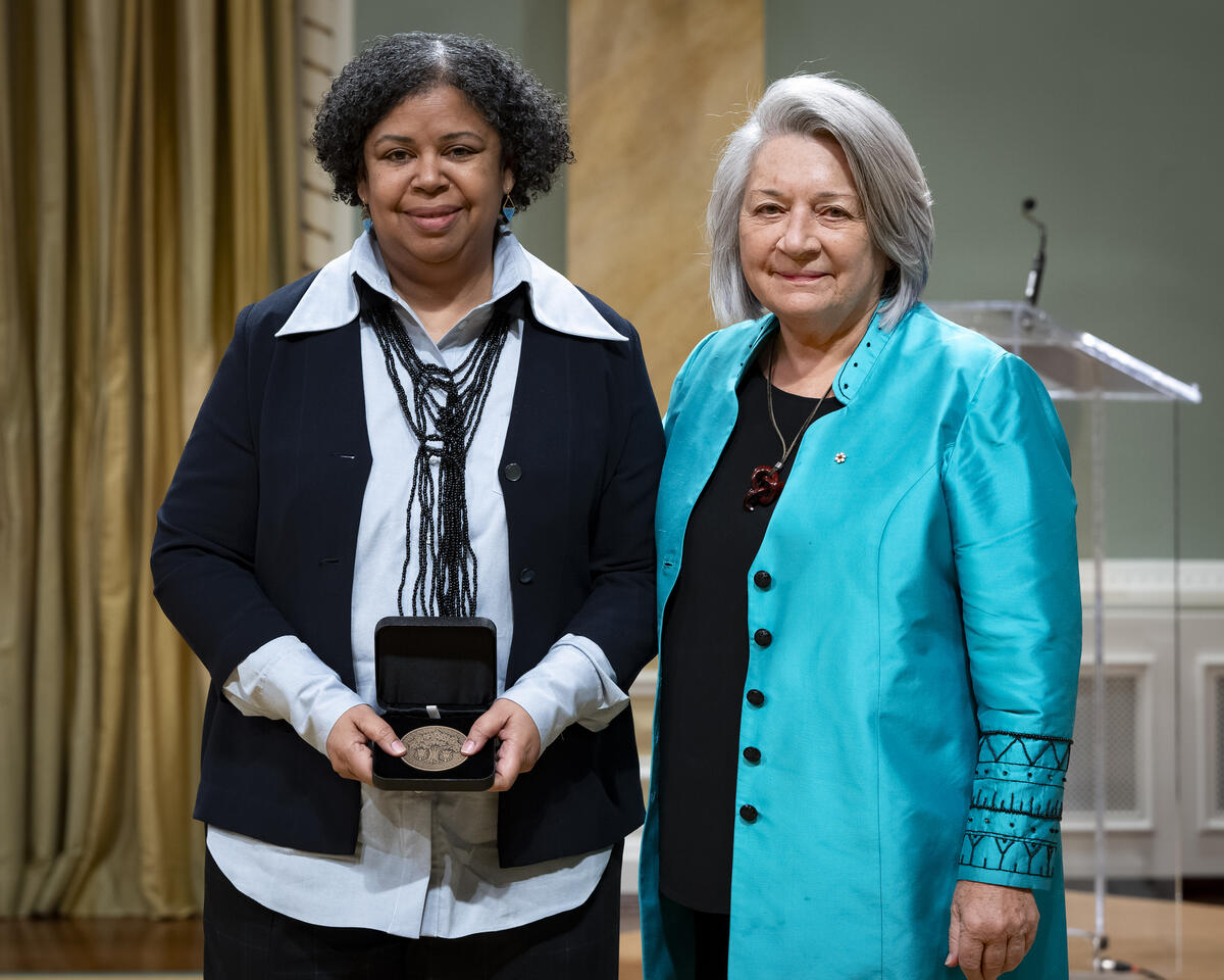 La gouverneure générale Mary Simons pose avec une dame qui tient un coffret de médailles ouvert.