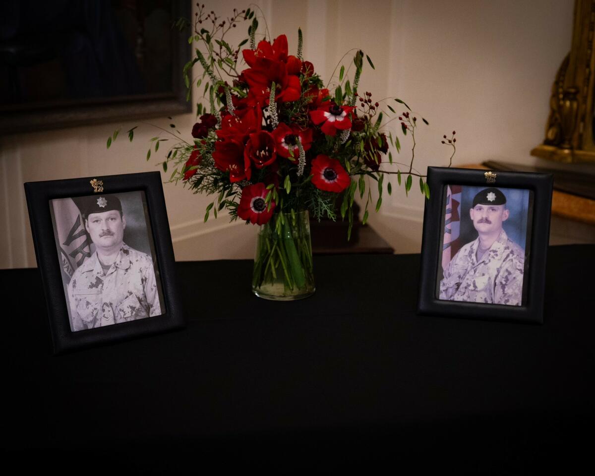 Deux photos de militaires sont exposées sur une table, de part et d'autre d'un vase contenant des fleurs rouges. La table est recouverte d'une nappe noire.