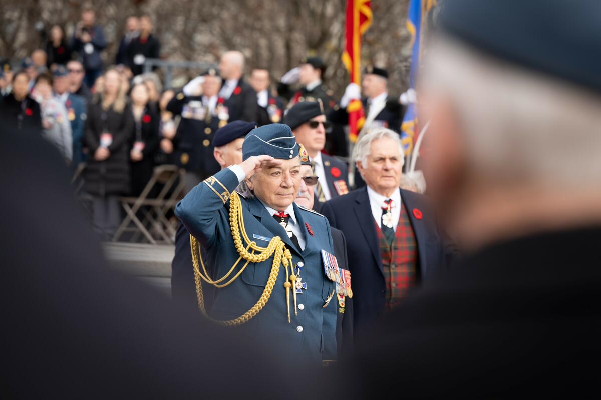 La gouverneure générale Mary Simon, portant l'uniforme de l'armée de l'air, salue. Une foule de personnes se trouve derrière elle. Son mari Whit Fraser est à sa droite.