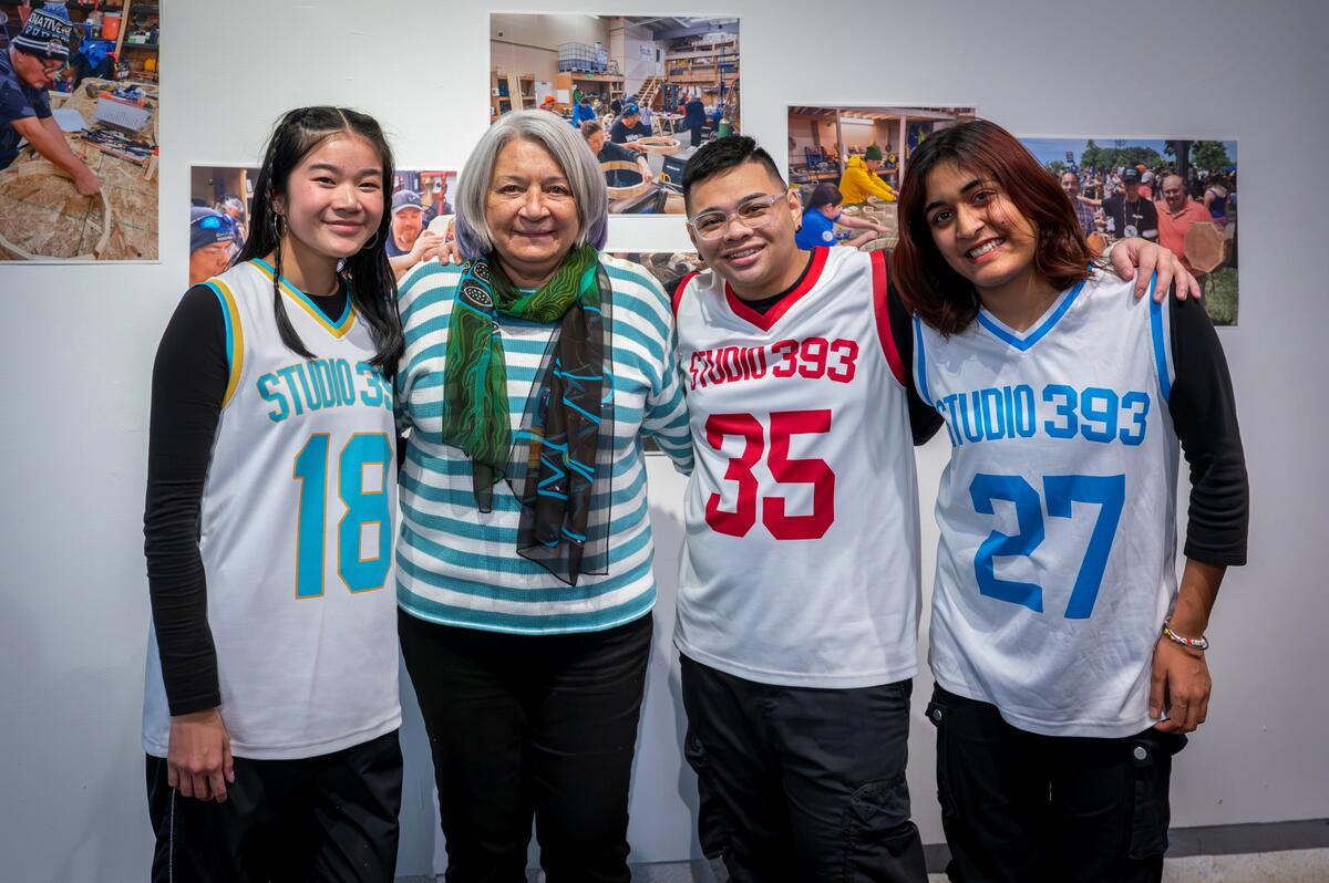 Three breakdancers wearing basketball gear are with Governor General Mary Simon, smiling for the camera.